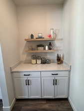 Bar area with white cabinetry, open shelves, light stone countertops, and dark wood-style flooring