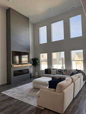 Living room featuring dark wood-style flooring, a large fireplace, and a high textured ceiling