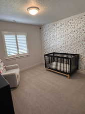 Bedroom with light carpet, a textured ceiling, and a nursery area