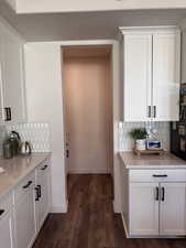 Kitchen featuring tasteful backsplash, white cabinets, dark wood finished floors, and light stone countertops