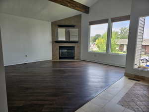 Unfurnished living room featuring lofted ceiling with beams, a large fireplace, and dark wood-style flooring