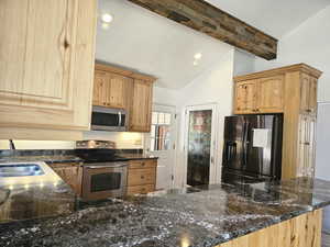 Kitchen with stainless steel appliances, dark stone countertops, recessed lighting, light wood finish cabinetry, and vaulted ceiling with beams