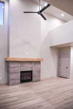 Unfurnished living room with wood finished floors, a tiled fireplace, a ceiling fan, vaulted ceiling, and recessed lighting