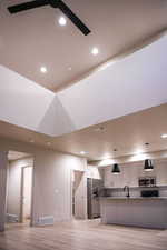 Kitchen with stainless steel appliances, open floor plan, hanging light fixtures, light wood finished floors, and a kitchen island with sink