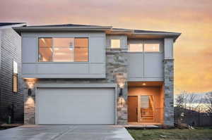 Contemporary home featuring stone siding, a garage, driveway, and stucco siding