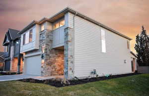 Property exterior at dusk with stone siding, an attached garage, driveway, and a yard