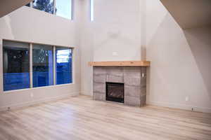 Unfurnished living room featuring a fireplace, wood finished floors, and a high ceiling