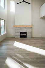 Unfurnished living room with wood finished floors, a high ceiling, a fireplace, and a ceiling fan