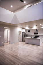 Kitchen with open floor plan, light countertops, an island with sink, hanging light fixtures, and a high ceiling
