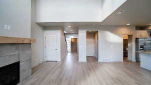 Unfurnished living room featuring a tiled fireplace, light wood-style flooring, recessed lighting, and a high ceiling