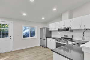 Kitchen featuring stainless steel appliances, white cabinetry, light wood finished floors, vaulted ceiling, and decorative backsplash