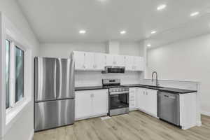 Kitchen with stainless steel appliances, white cabinets, light wood finished floors, decorative backsplash, and vaulted ceiling