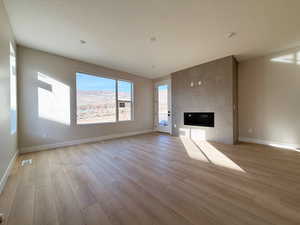 Unfurnished living room with a tiled fireplace, light wood-style flooring, and a textured ceiling