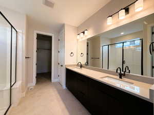 Full bath with a shower stall, double vanity, light tile patterned floors, and a walk in closet