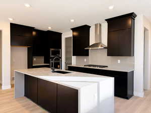 Kitchen featuring dark cabinets, modern cabinets, light stone countertops, light wood-style flooring, and a center island with sink