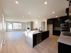 Kitchen with dark cabinets, an island with sink, light stone counters, stainless steel appliances, and a textured ceiling