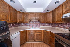 Kitchen with electric stove, wood finish cabinets, white dishwasher, a textured ceiling, and light countertops