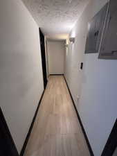 Corridor featuring electric panel, a textured ceiling, and light wood-type flooring