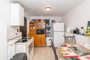 Dual tone kitchen featuring white appliances, a textured ceiling, two tone color scheme, light tile patterned floors, and light countertops