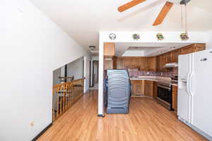 Kitchen featuring white refrigerator with ice dispenser, stainless steel electric range oven, light countertops, backsplash, and wood finish cabinetry