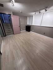 Finished below grade area featuring track lighting, light wood-type flooring, and a textured ceiling