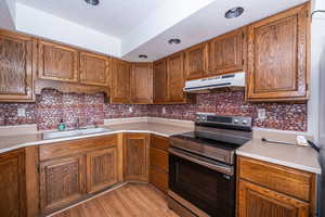 Kitchen with stainless steel electric range oven, light countertops, wood finish cabinets, and a textured ceiling