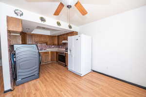Kitchen with white fridge with ice dispenser, light countertops, tasteful backsplash, a ceiling fan, and light wood-type flooring