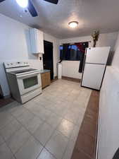 Kitchen with white appliances, a textured ceiling, white cabinets, light tile patterned floors, and light countertops