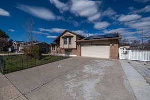 Tri-level home with solar panels, a gate, brick siding, concrete driveway, and a garage