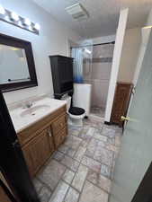 Bathroom with vanity, a shower stall, a textured ceiling, and light stone finish flooring