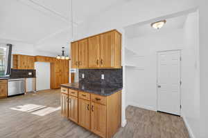 Kitchen featuring open shelves, stainless steel dishwasher, hanging light fixtures, tasteful backsplash, and dark stone countertops