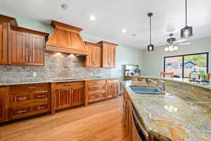 Kitchen featuring light stone countertops, pendant lighting, light wood-style flooring, a ceiling fan, and wood finish cabinets