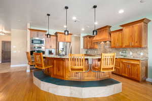 Kitchen featuring a kitchen bar, light stone counters, wood finish cabinetry, and hanging light fixtures