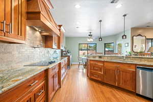 Kitchen with wood finish cabinetry, light stone counters, stainless steel dishwasher, light wood finished floors, and ceiling fan