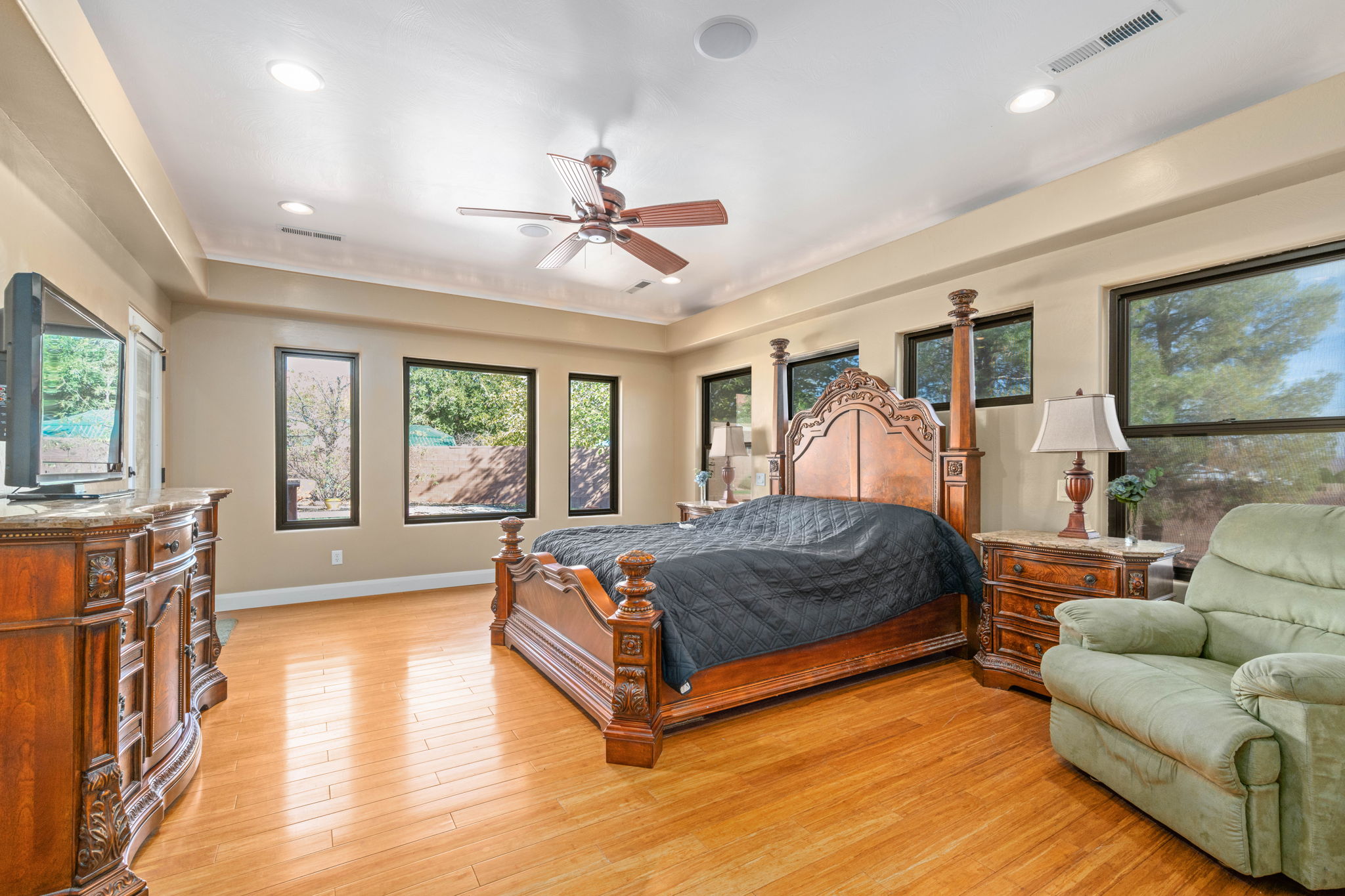 Bedroom featuring multiple windows, light wood-type flooring, ceiling fan, and a tray ceiling