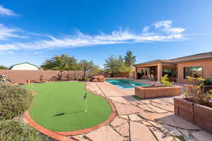 View of swimming pool with a putting green, patio surround, and a fenced backyard