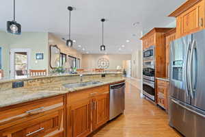 Kitchen featuring stainless steel appliances, wood finish cabinetry, light stone countertops, and hanging light fixtures