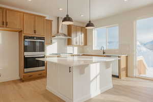 Kitchen featuring stainless steel appliances, light wood-style flooring, pendant lighting, a kitchen island, and a breakfast bar