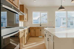 Two tone kitchen with stainless steel appliances, light wood finished floors, backsplash, pendant lighting, and dual tone cabinets