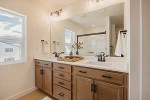 Full bath with double vanity, a shower stall, and light wood-style flooring