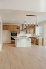 Kitchen featuring a breakfast bar, light wood finished floors, stainless steel appliances, a kitchen island, and decorative light fixtures