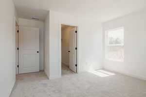 Unfurnished bedroom with light carpet and a spacious closet