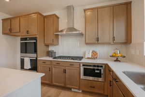 Kitchen with stainless steel appliances, wood finish cabinets, light wood-style flooring, and light stone countertops