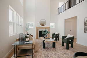 Living room featuring a tiled fireplace, light wood-style floors, plenty of natural light, and a high ceiling