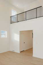 Empty room with a high ceiling, plenty of natural light, and light wood finished floors