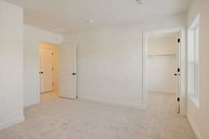 Unfurnished bedroom with a walk in closet and light colored carpet