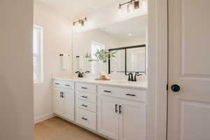 Full bath with double vanity, a shower stall, and light wood-type flooring