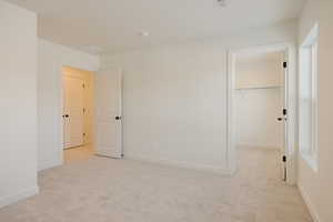 Unfurnished bedroom featuring a walk in closet and light carpet