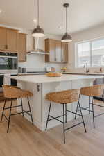 Kitchen with a kitchen breakfast bar, light wood finished floors, stainless steel appliances, a center island, and hanging light fixtures