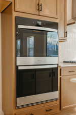 Kitchen with stainless steel double oven, light wood finish cabinets, light countertops, and backsplash